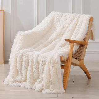 A cream fluffy faux fur throw blanket on a rattan chair