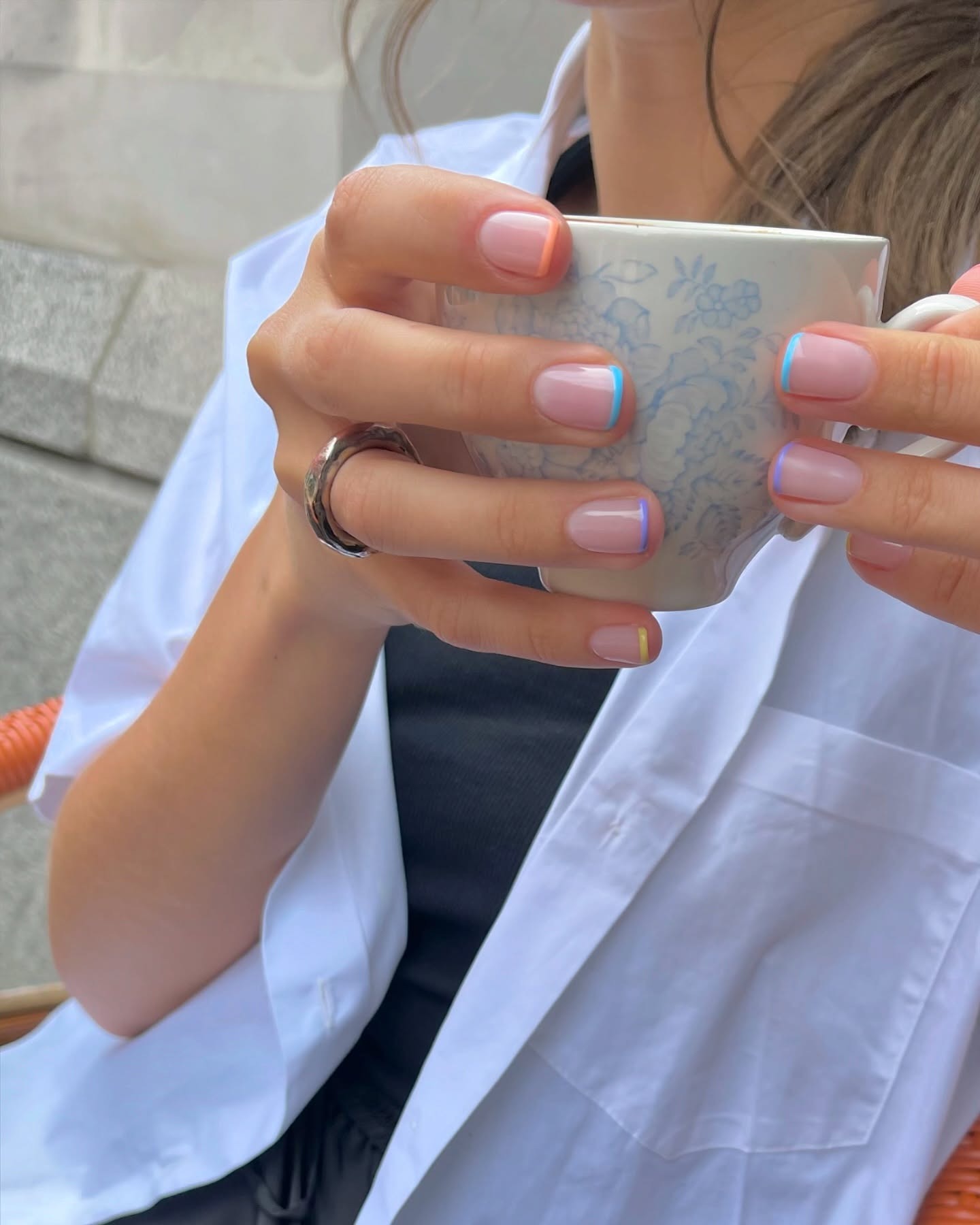 A woman holding a mug with a colourful French tip manicure