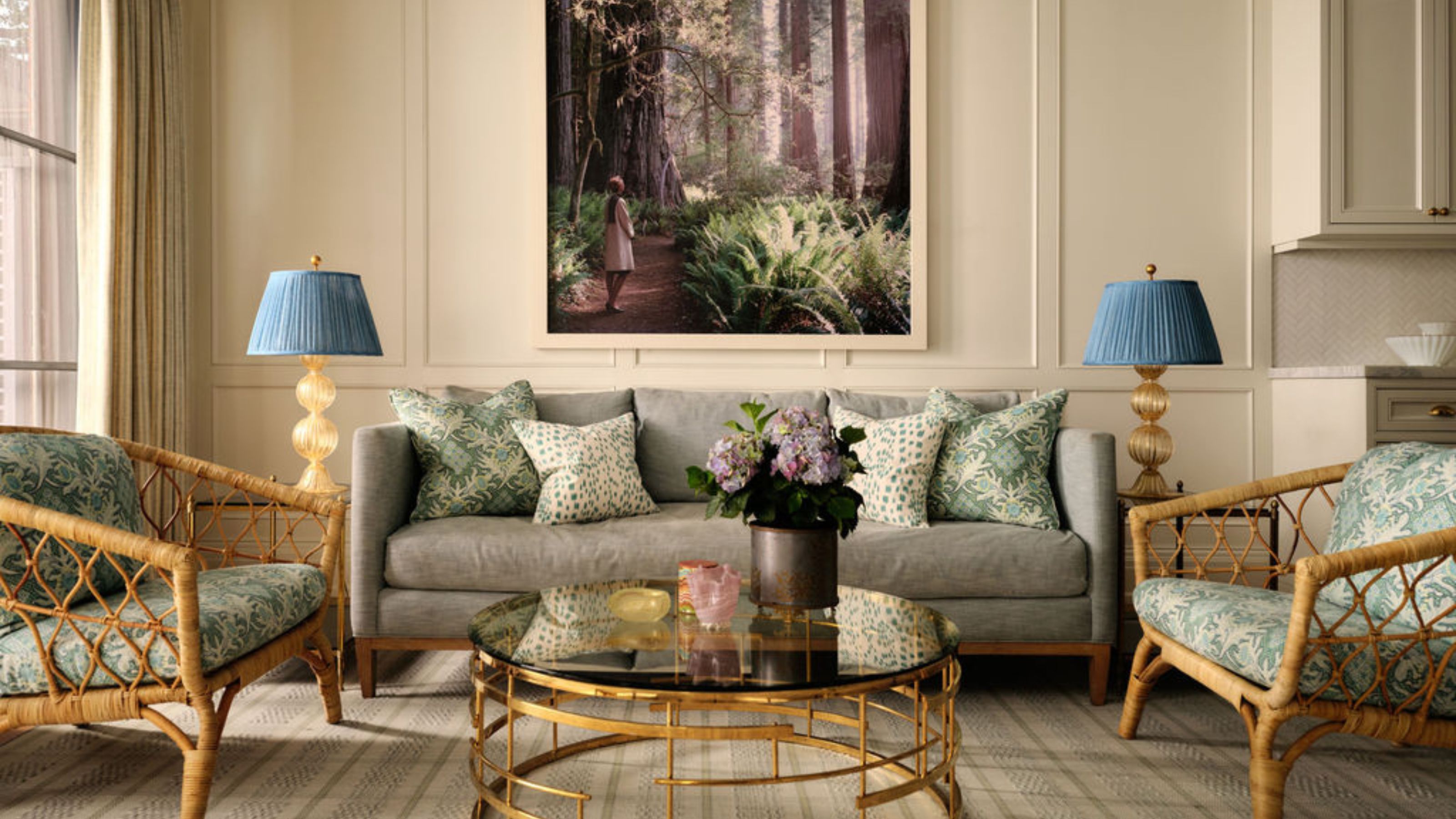 a cozy neutral family room off the kitchen with paneled walls, a large couch, rattan side chairs and a brass coffee table