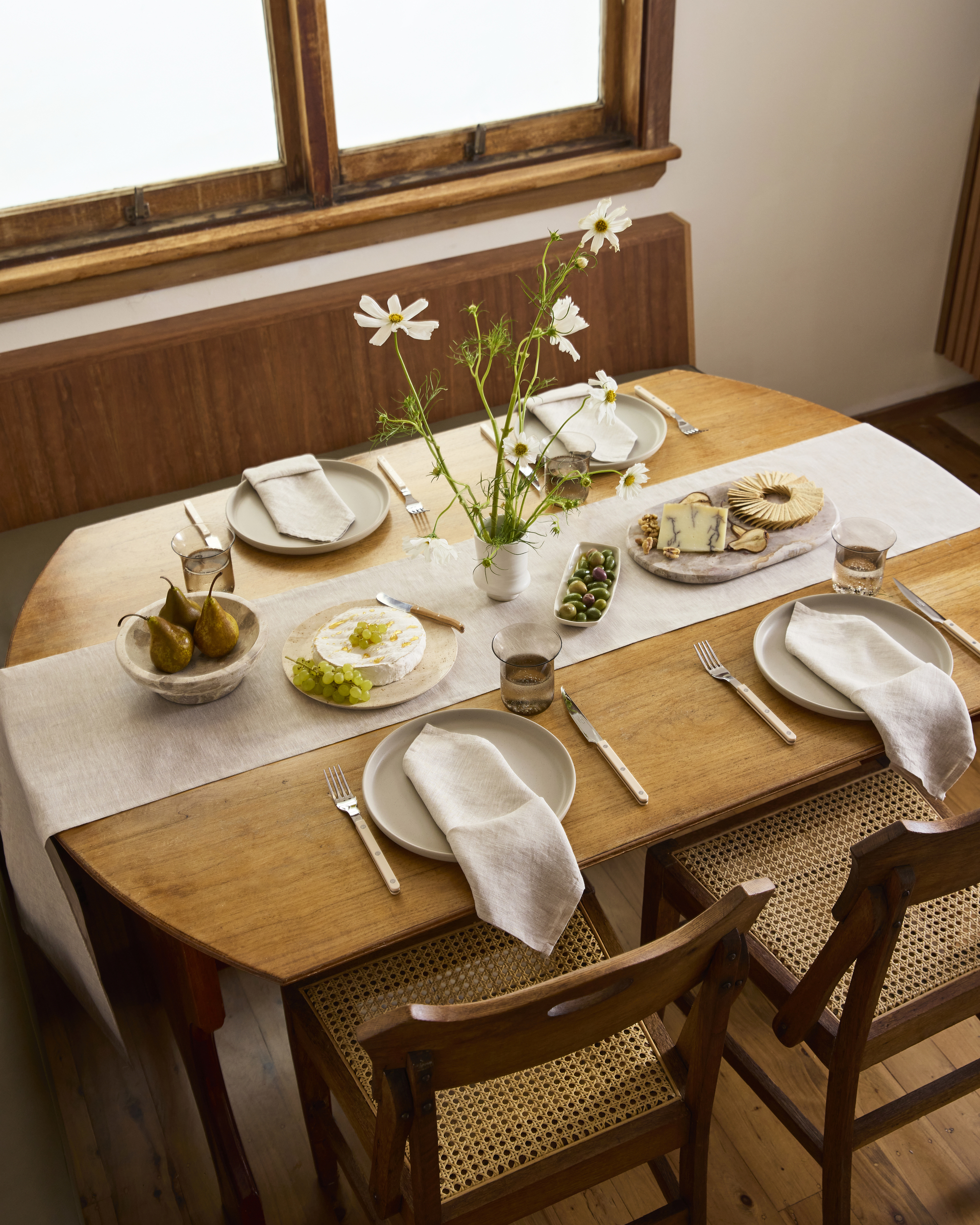 Image of a wooden table with an off-white table runner on it that is set with plates and food.