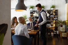 Image of sommelier presenting wine to guests at a restaurant.