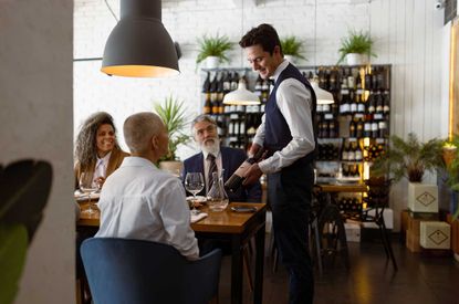 Image of sommelier presenting wine to guests at a restaurant.