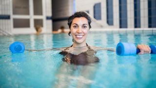 Woman holding two foam weights doing acqua aerobics at home