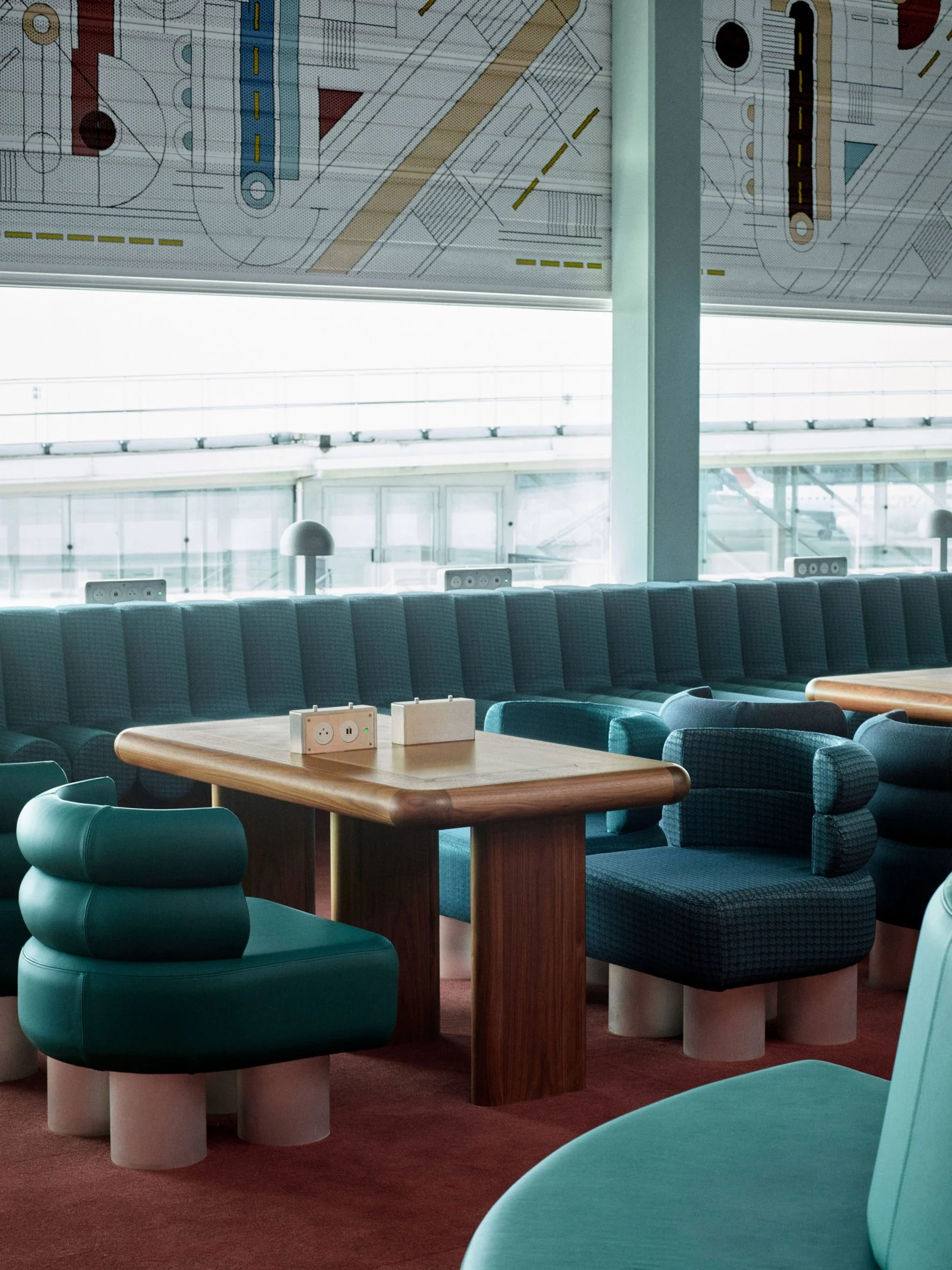 Close up of curved tubular chairs in teal around a sleek wooden table in an airport terminal