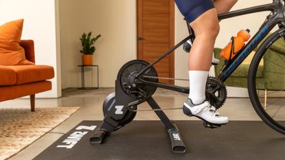 The Zwift Hub One smart trainer mounted on a bike and being ridden in a house