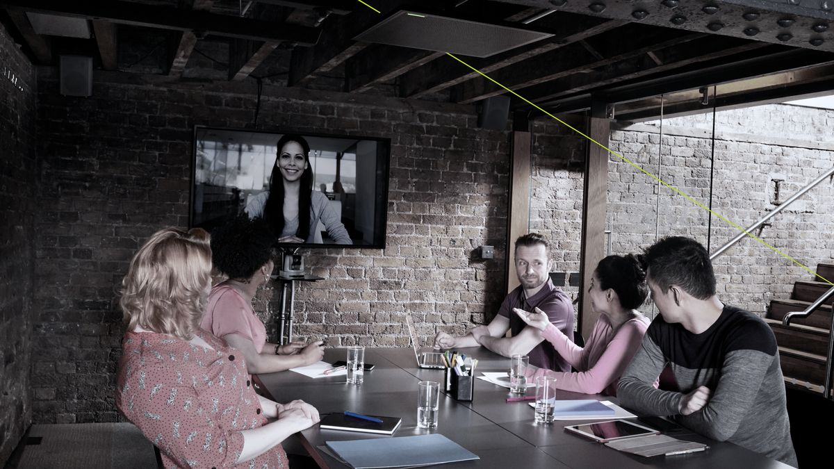 People sat at table in brick-walled meeting room with colleague on wall-mounted screen