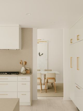 White kitchen with gold hardware, light wood floor and beige backsplash
