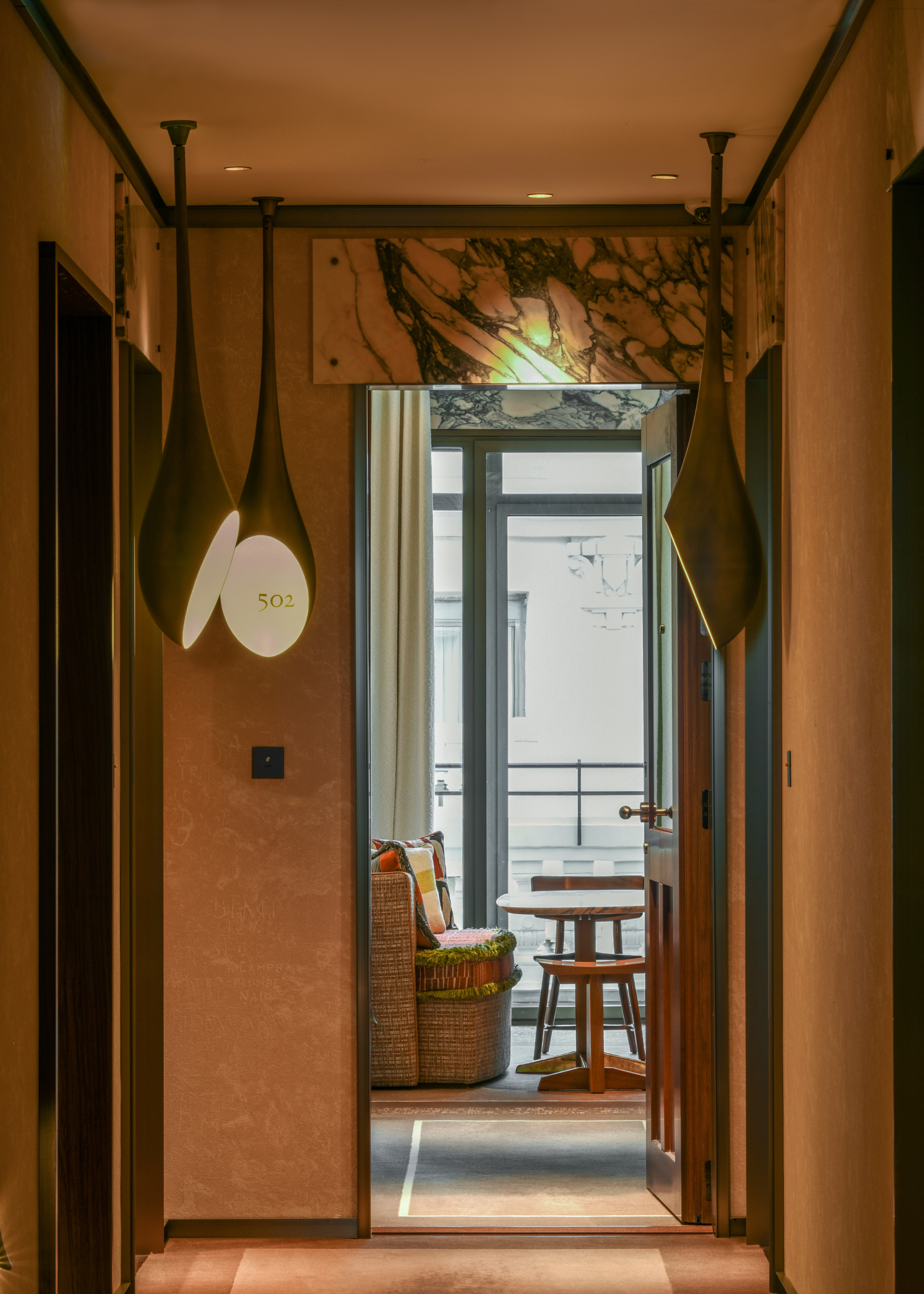 A hallway leading into a bedroom with a hanging pendant light with engraved room numbers