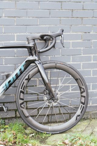 A black bike with deep black wheels against a dark grey brick wall.