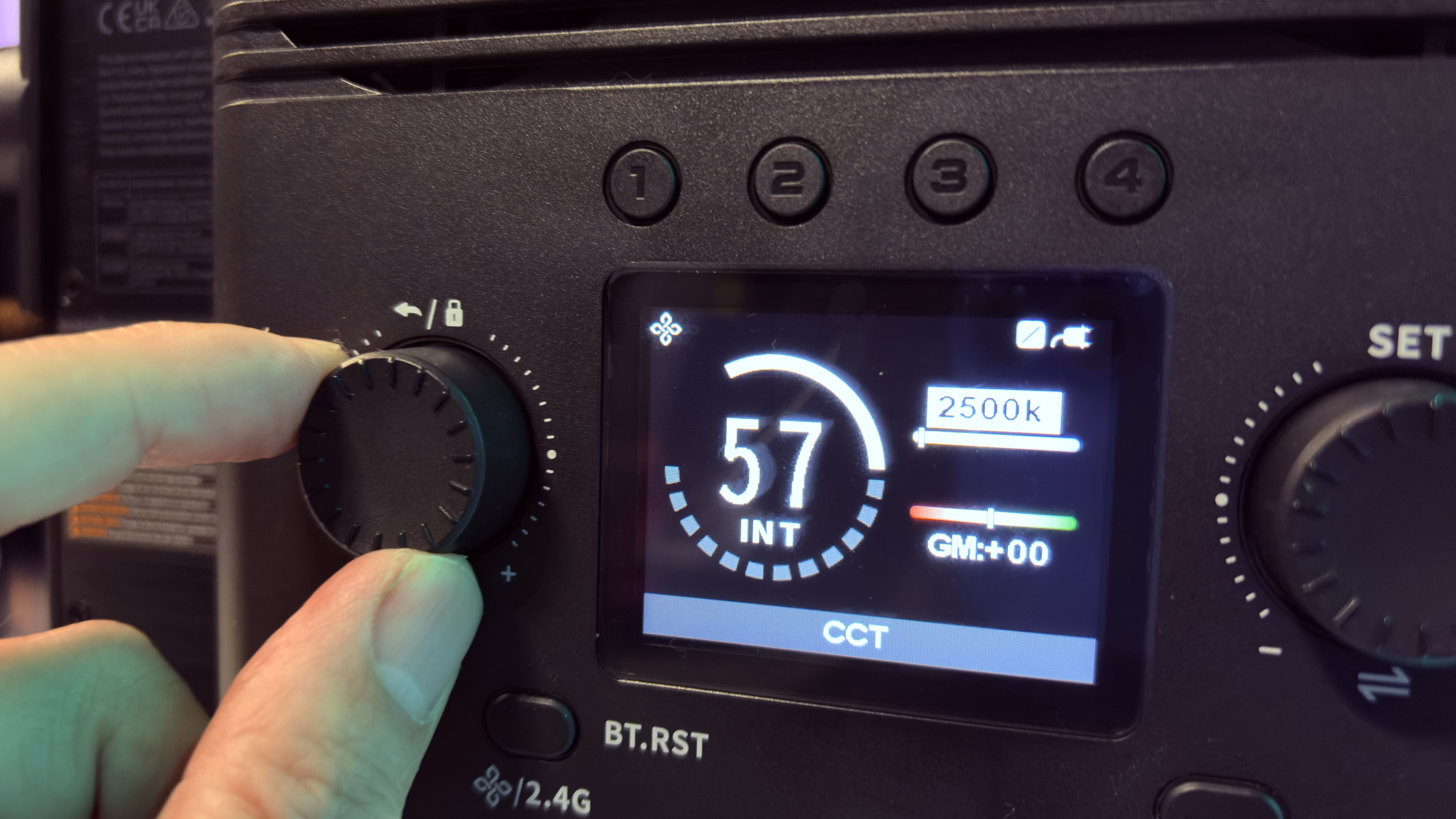 Close-up of  a hand twiddling the left knob on the rear of the LED, with the display showing the intensity off the HSI mode set to a level of 58