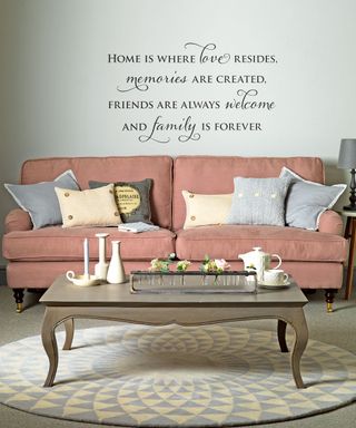 living area with white wall with quote and pink sofa and coffee table