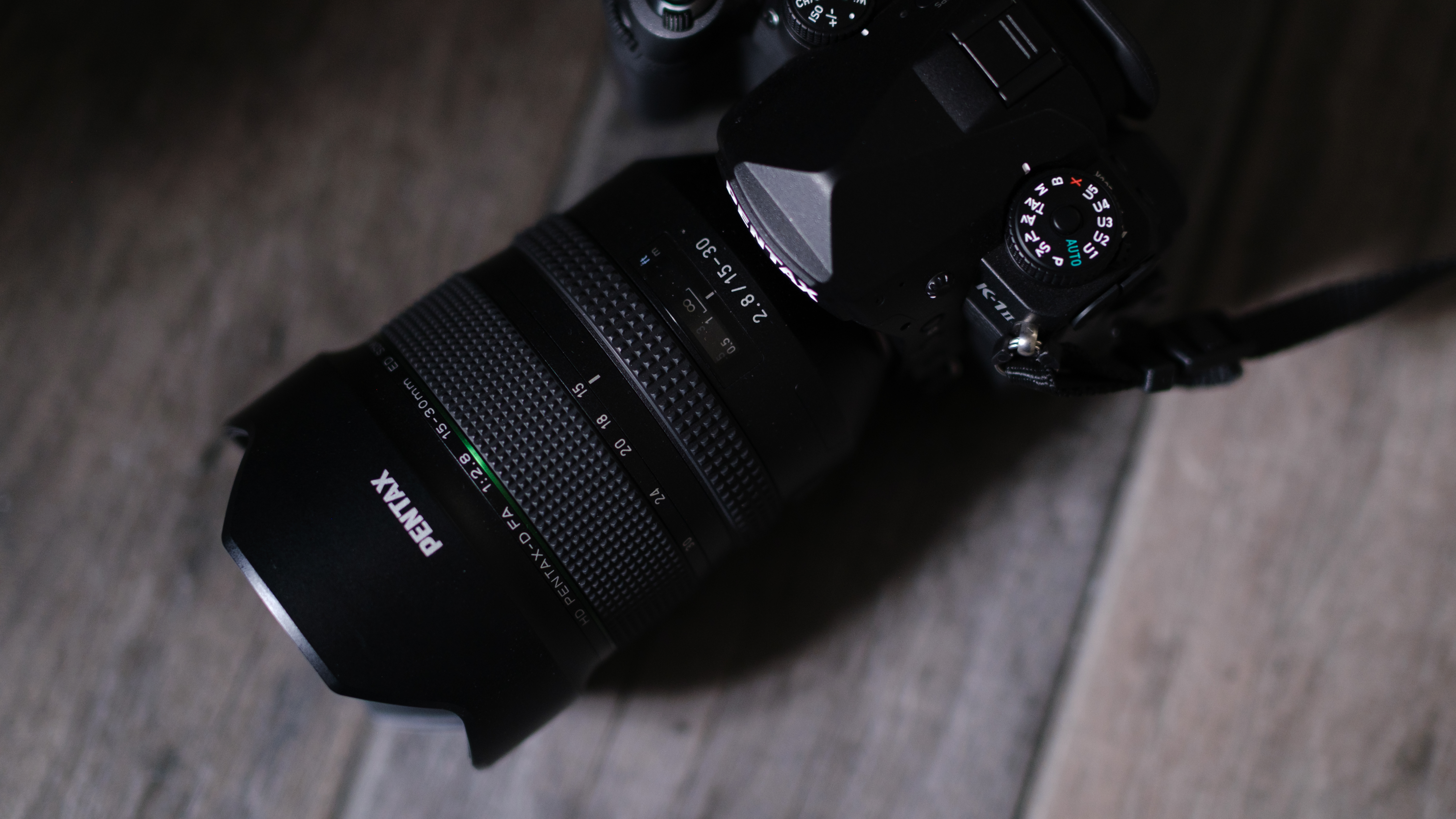 The Pentax-D FA 15-30mm f/2.8 ED SD WR on a gray wood background