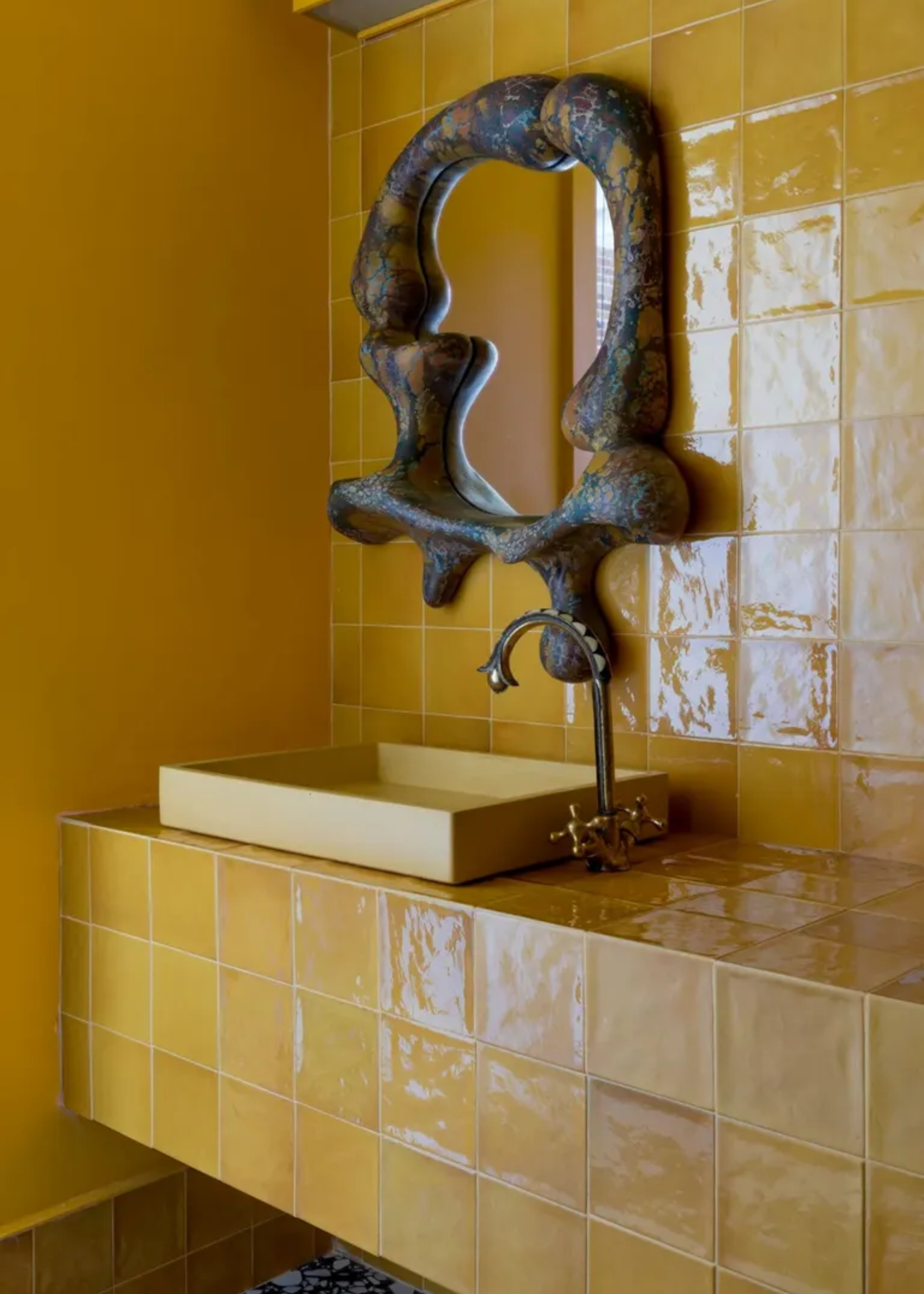 A bathroom with glossy yellow styles, a yellow sink, a silver tap, and a statement stone mirror