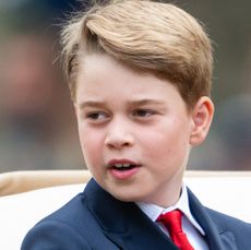 Prince George wearing a blue suit and red tie looking to the side