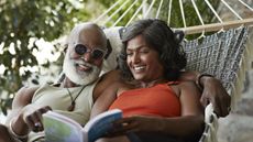 An older couple relax together in a hammock and read.