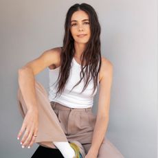 a portrait of the stylist Molly Dickson sitting on a stool and wearing a white tank top with khaki pants