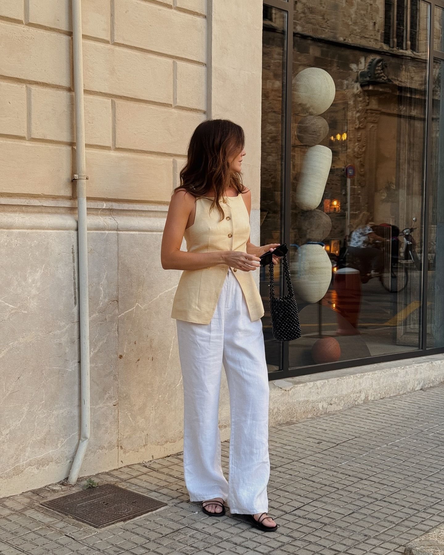 Woman wears yellow waistcoat, white linen trousers and black sandals