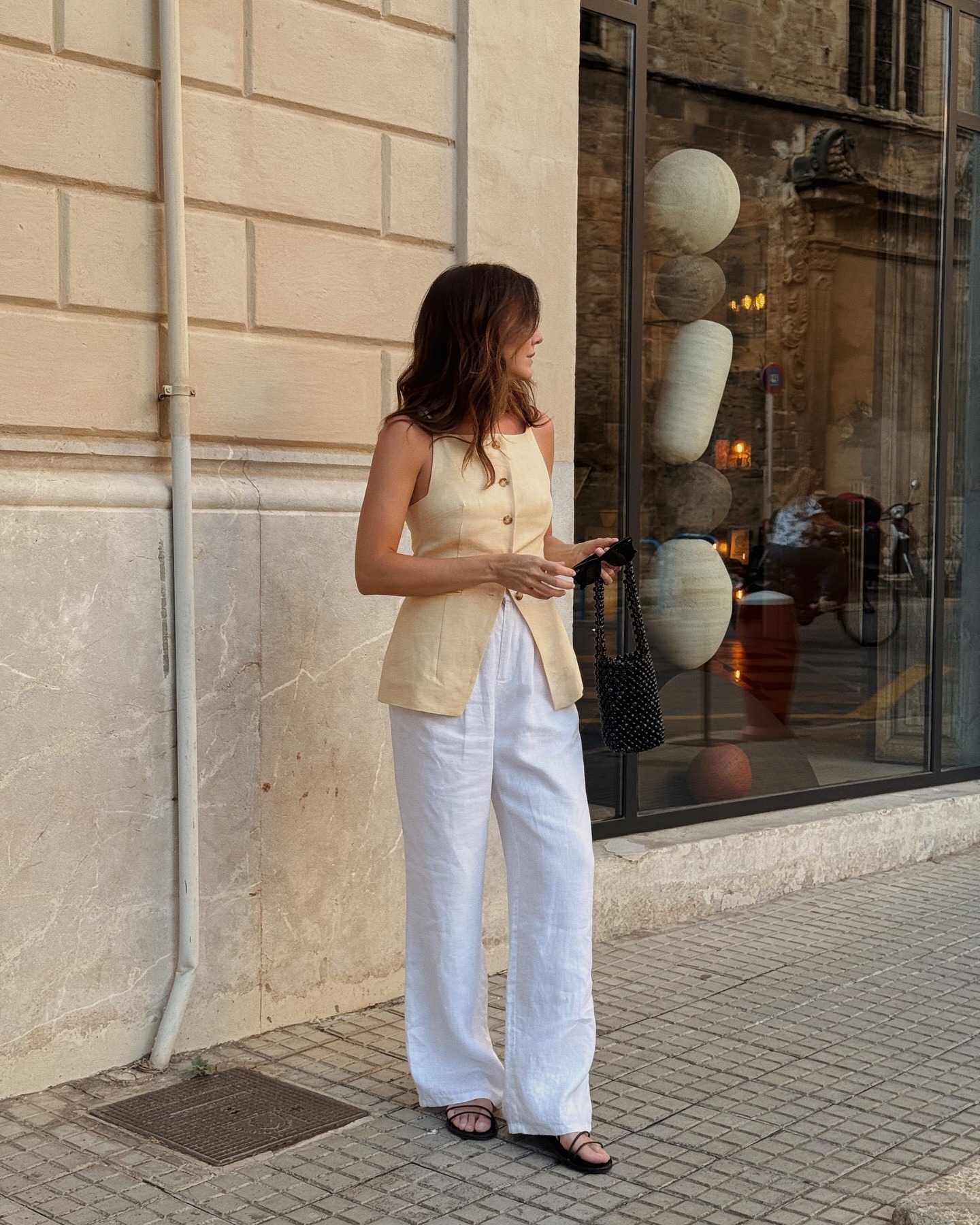 Woman wears yellow waistcoat, white linen trousers and black sandals