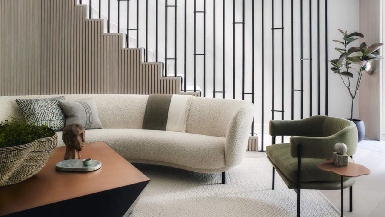 White, curved boucle sofa in a modern living room with an olive green velvet accent chair to the right of it and a brown metallic coffee table