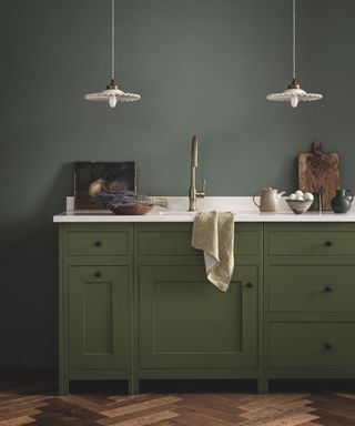 green kitchen cabinets with wooden herringbone floor and green walls