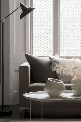 living room with neutral scheme, gray sofa, white coffee table, black floor lamp, window film, white ceramic vases