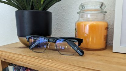 The Lucyd Lyte glasses next to a plant and a yellow candle sat on a bookshelf