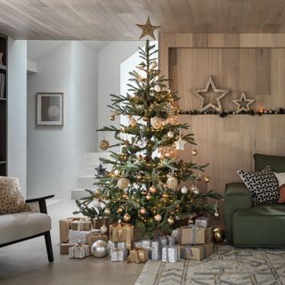 An artificial Christmas tree surrounded by gifts in a wooden panelled room