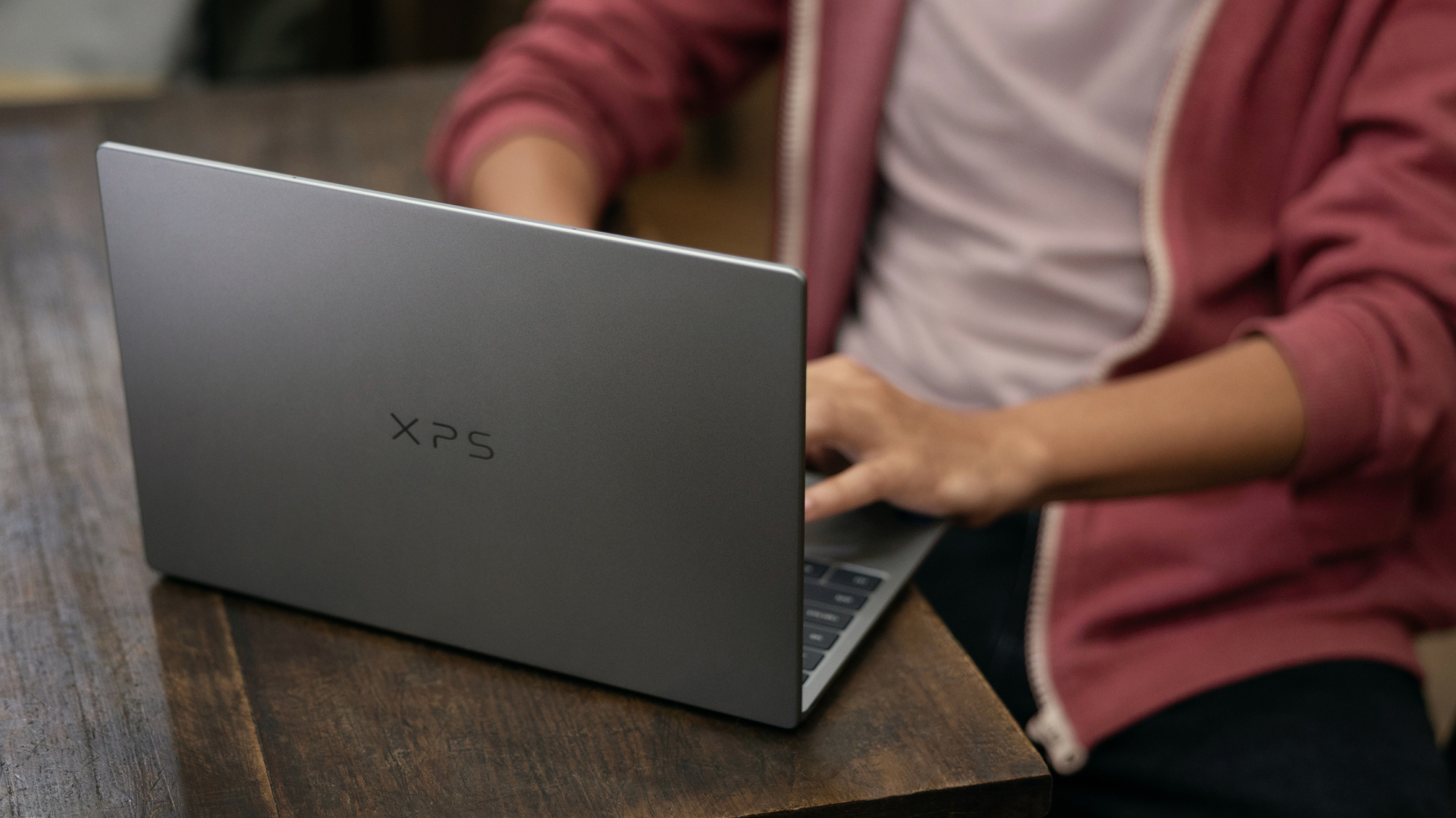 Dell XPS 13 being used by a person at a desk, laptop is viewed from the rear and you can see the XPS logo on the lid