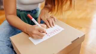woman writing 'fragile' label on to of a storage box