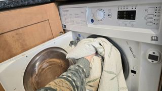 A Tom's guide tester placing the Utopia Bedding Bamboo mattress protector in a white washing machine