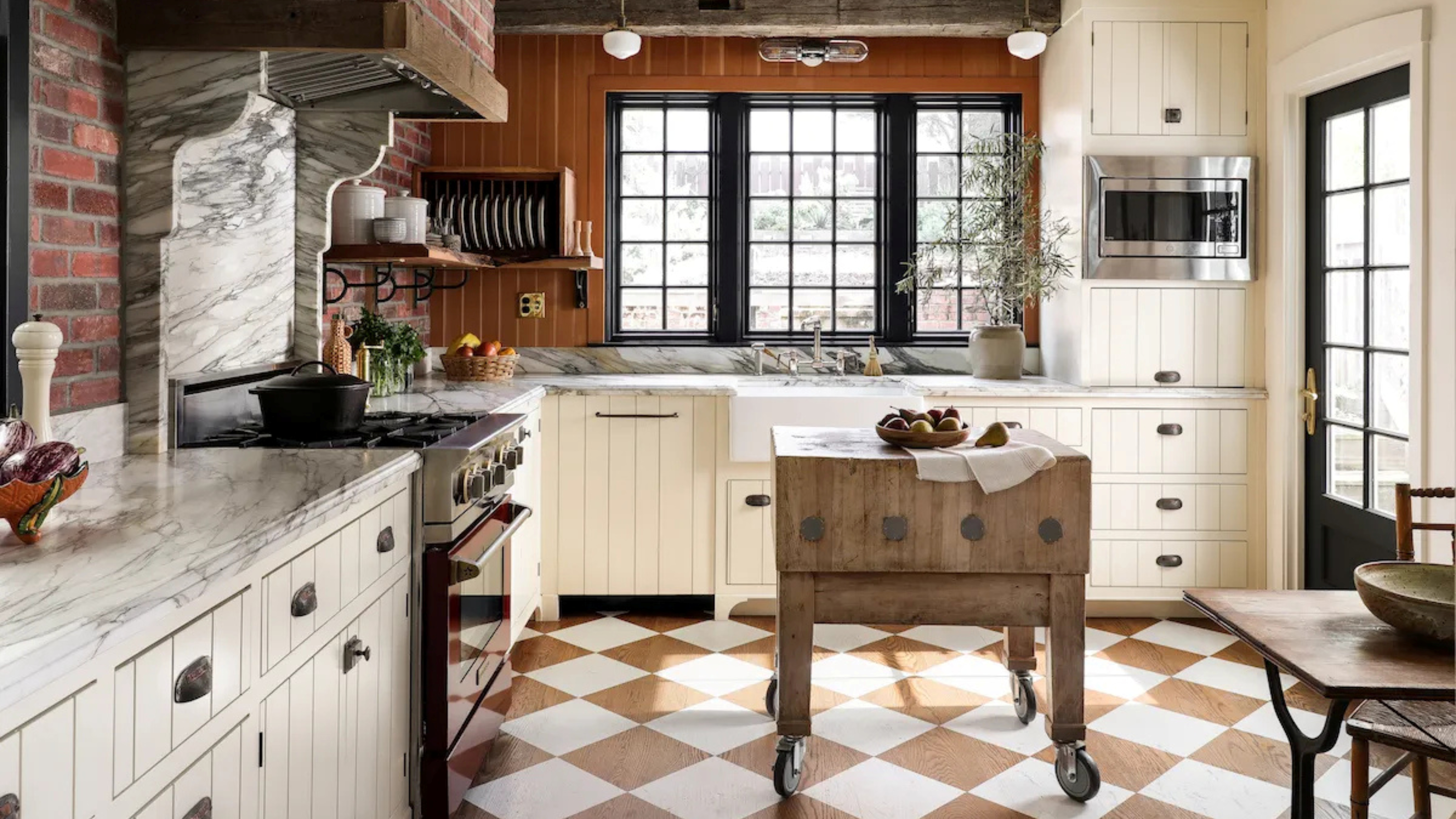 Country kitchen with cream cabinets and a checkerboard wood and white floor with a vintage butchers block