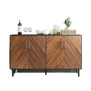 A dark brown wooden sideboard with four doors, a bottle, two wine glasses, white bowls, and plants on top of it