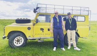 A yellow Land Rover with Cleeve Hill on it and two men stand in front of it