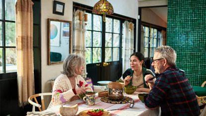 Older parents with adult daughter sitting at table eating meal together