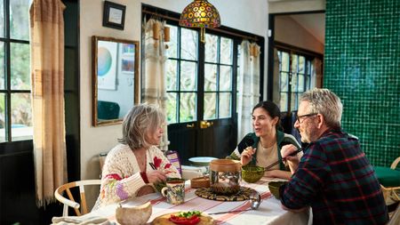 Older parents with adult daughter sitting at table eating meal together