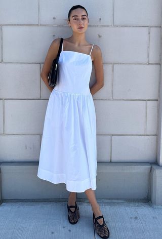 a photo of a woman's white dress outfit with a poplin frock styled with black mesh fishnet flats and a black shoulder bag