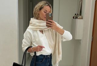  @anoukyve wearing a white sweater, white scarf, jeans, boots, and a black bag.