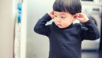 a young child at a doctor's office holds his ears with his hands