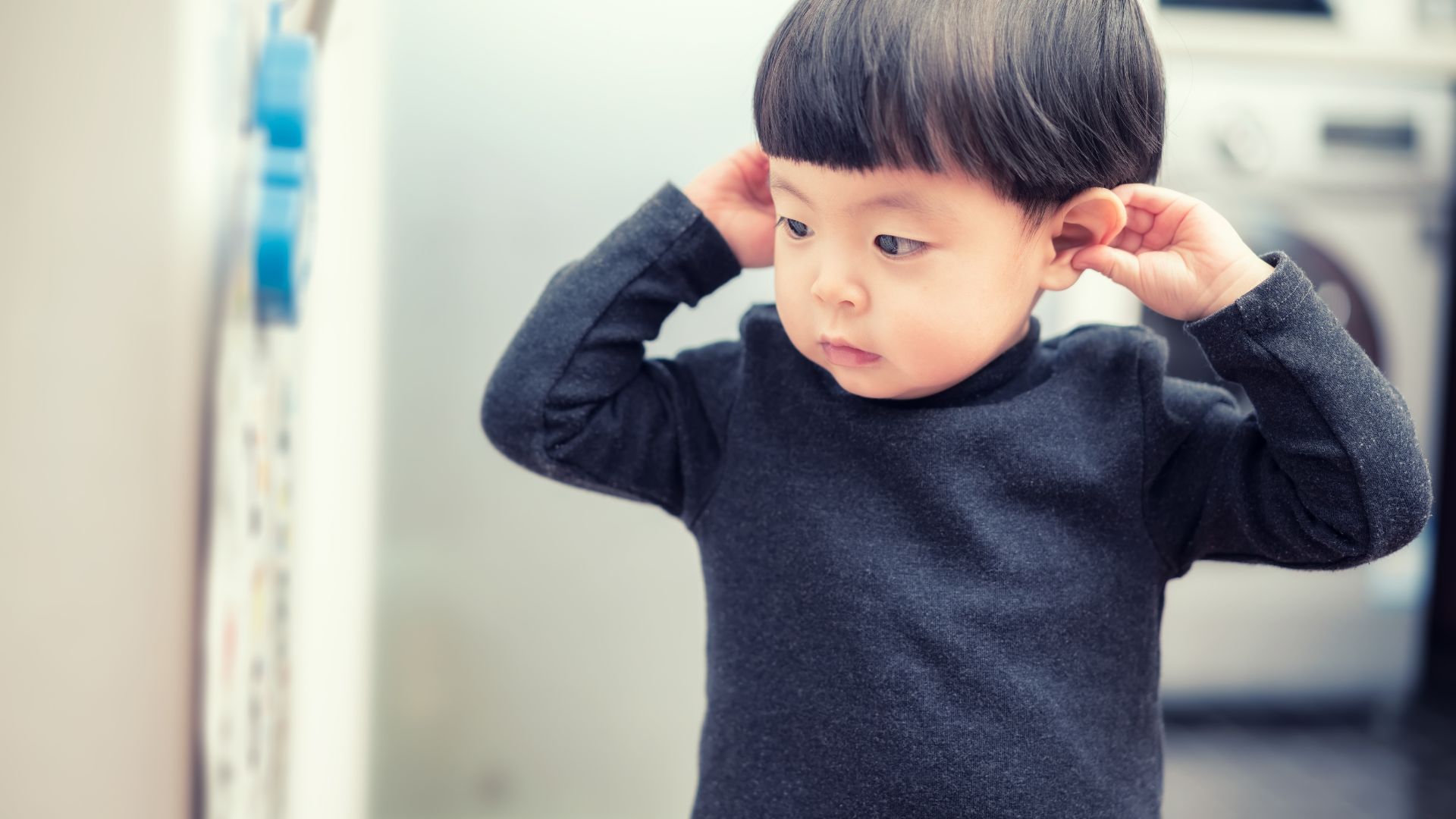 a young child at a doctor's office holds his ears with his hands