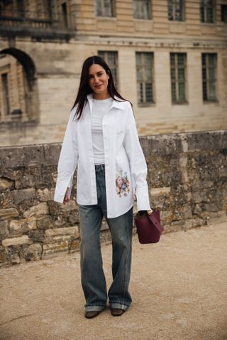 a guest attends paris spring summer 2025 fashion week wearing a big white button down shirt and baggy jeans