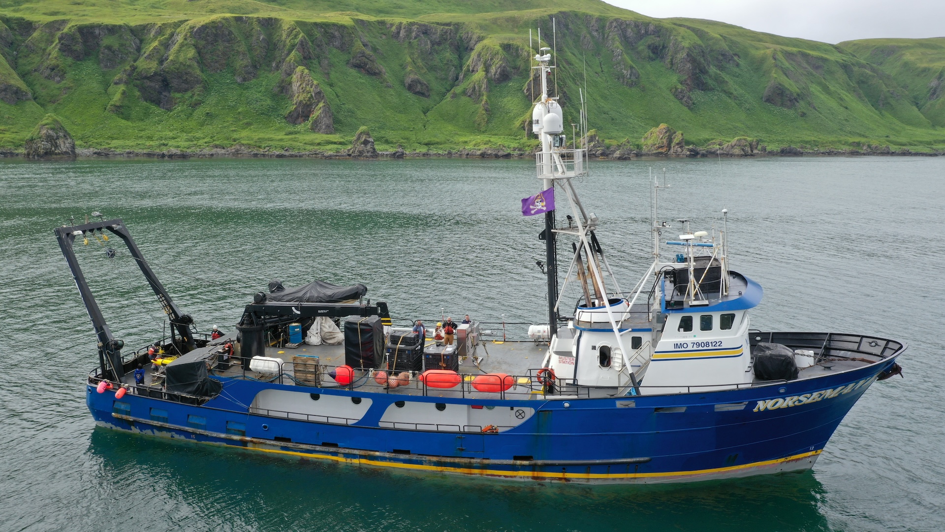 A photo of a blue mid-sized ship near a green hilly shore