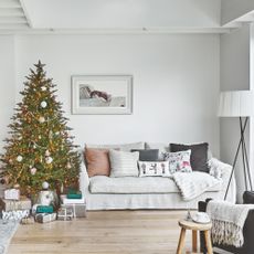 Grey sofa with cushions on it, next to a christmas tree with presents underneath it