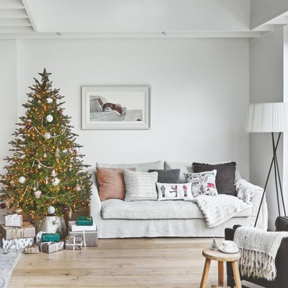 Grey sofa with cushions on it, next to a christmas tree with presents underneath it