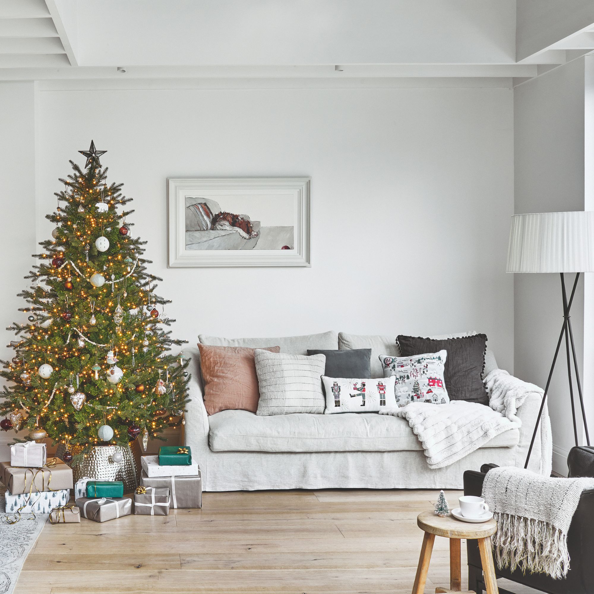 Grey sofa with cushions on it, next to a christmas tree with presents underneath it