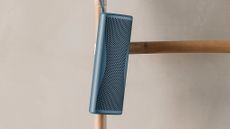 KEF Muo 2025 Bluetooth speaker in blue, hanging from a bamboo bathroom towel rack