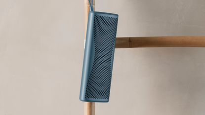 KEF Muo 2025 Bluetooth speaker in blue, hanging from a bamboo bathroom towel rack