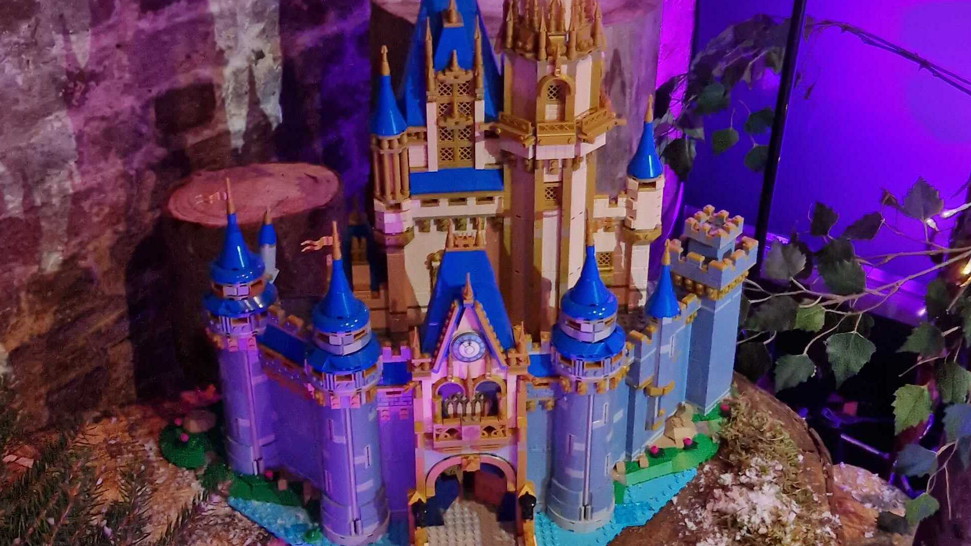 The Lego Disney Castle set up on a log, against a brick background with purple mood lighting