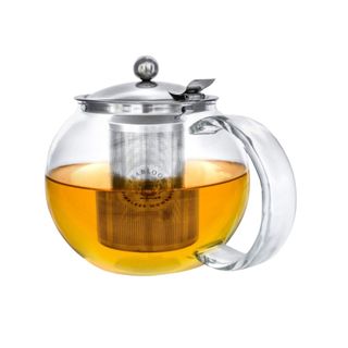 A glass teapot with a silver lid and a silver tea strainer and orange tea inside it