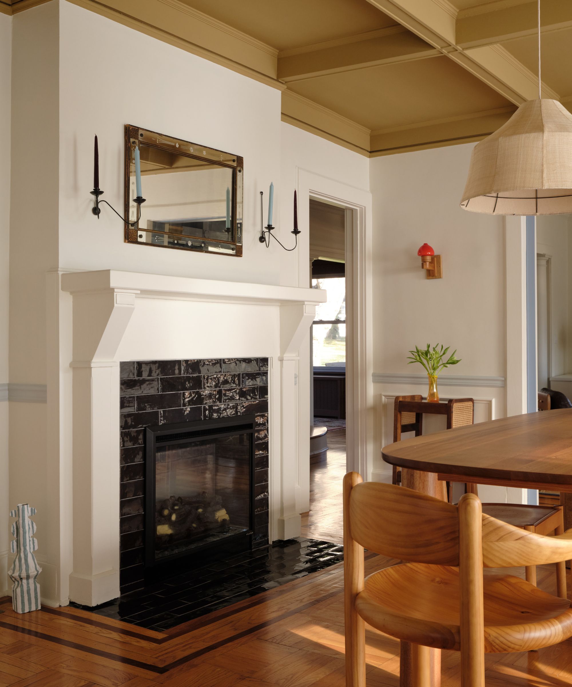 a serene white painted dining room with a painted wooden fireplace and a butter yellow accent ceiling with warm pine floors and table and chairs