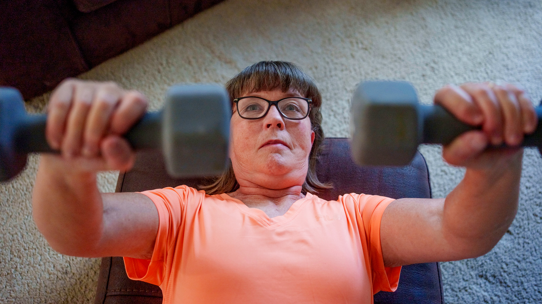 Woman exercises with dumbbells at home, lying on her back on an exercise mat on a carpeted floor